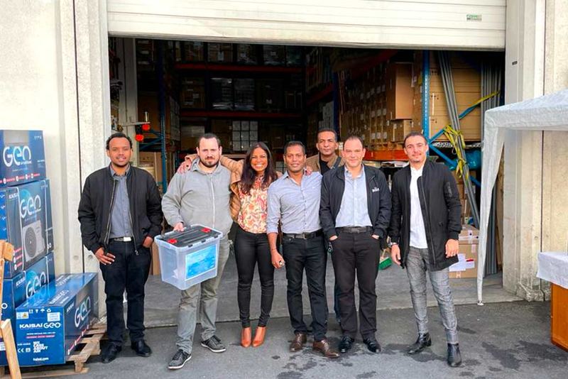 L’équipe HEROSYSTEME, sept personnes devant la porte ouverte de l’entrepôt, cartons de climatiseurs Kaisai à gauche