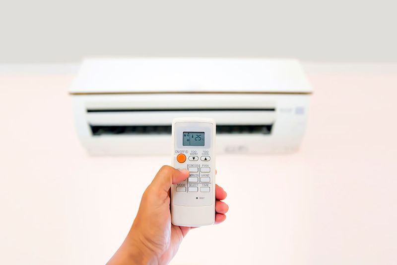 Main réglant un climatiseur mural avec sa télécommande