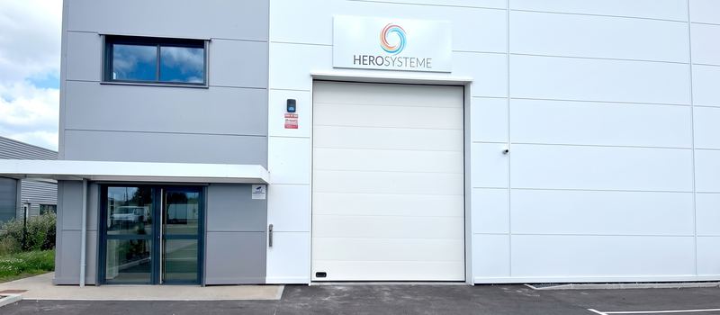 Façade de HEROSYSTEME : enseigne au logo au-dessus de la porte sectionnelle, entrée vitrée à gauche