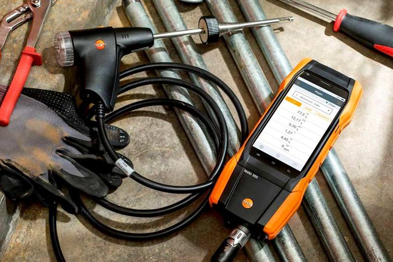 Analyseur de combustion testo 300 et sa sonde posés sur des tubes, à côté de gants et d’outils