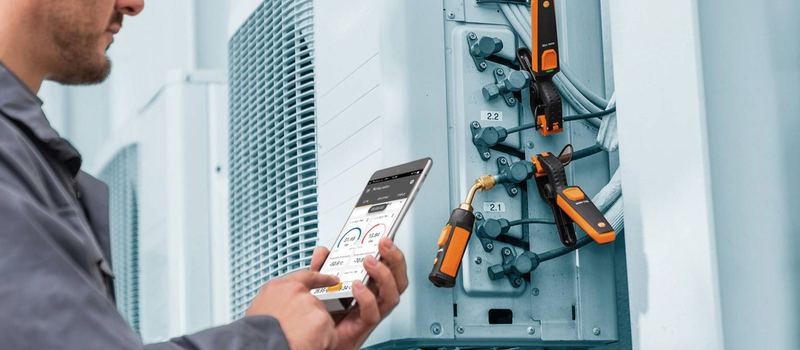 Technicien lisant sur son smartphone les mesures de sondes testo fixées sur une unité extérieure