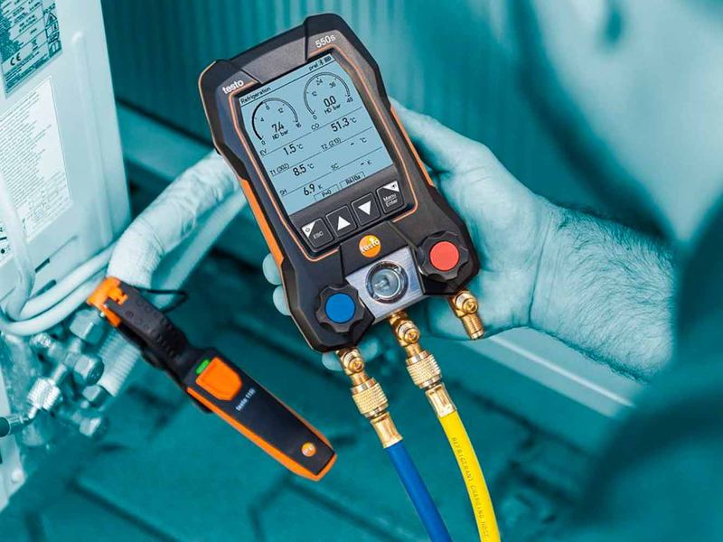Manifold électronique testo 550s tenu en main, avec ses flexibles et sa pince de température